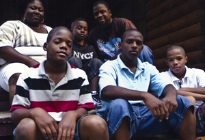 Group of seven young men sitting on wooden steps outside a building, posing for a photo.